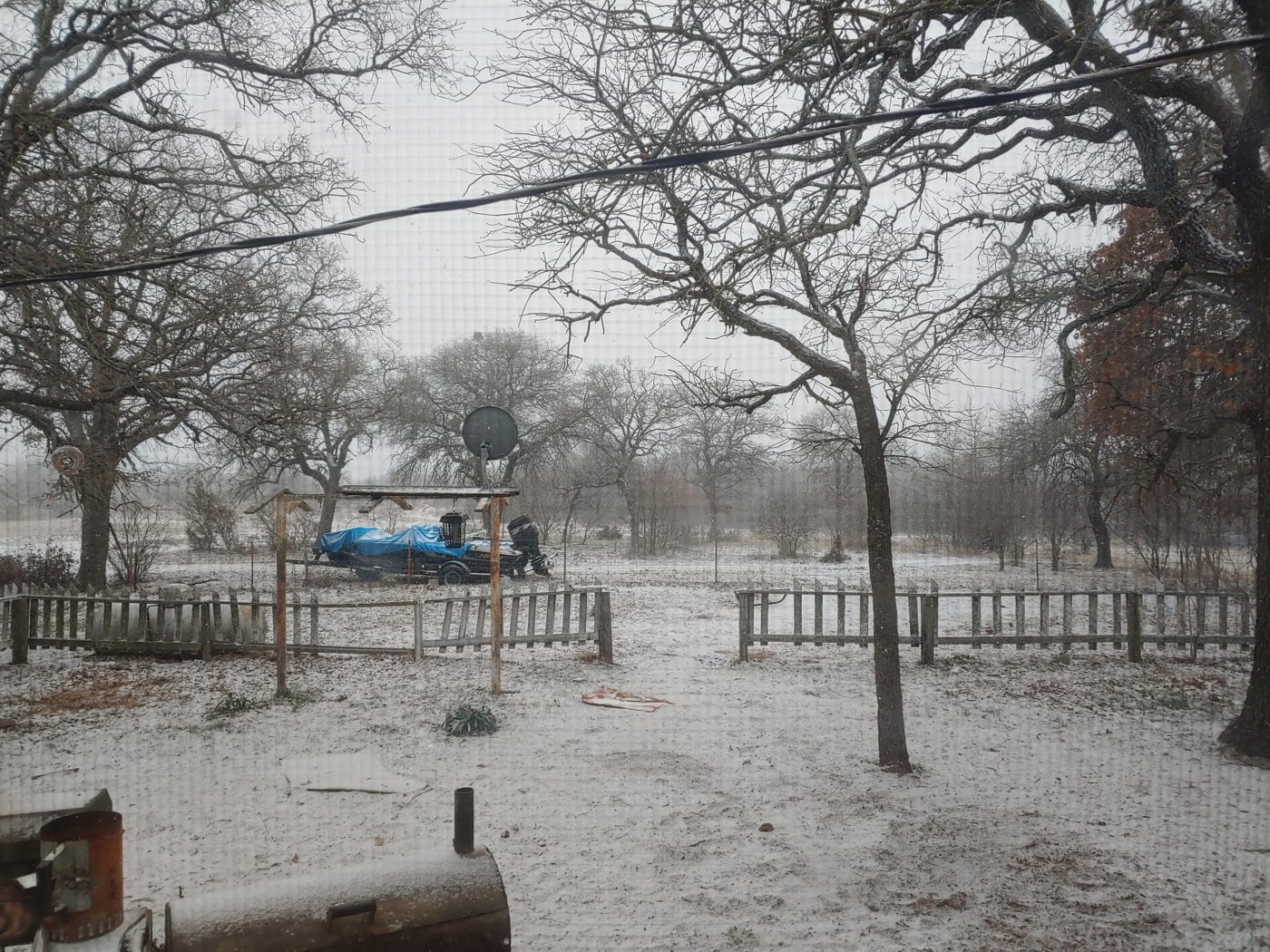 Snow and ice covering our North Central Texas backyard during Winter Storm Uri on February 14, 2021, with bare oaks, a fence line, and a tarp-covered boat